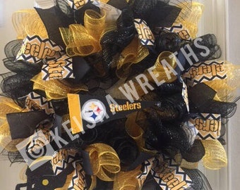 Könnte beinhalten: Ein dekorativer Kranz mit schwarzen und goldenen Bändern und Akzenten. Der Kranz enthält einen Footballhelm und ein Banner mit dem Text "Steelers". Der Kranz ist ein Fanartikel.