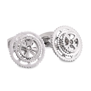 May include: A pair of silver cufflinks featuring a gear design. The cufflinks are made of metal and have a polished finish.