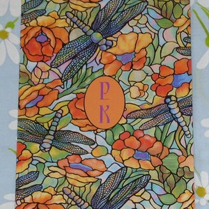 May include: A colorful stained glass design featuring dragonflies and flowers. The design is in shades of orange, yellow, blue, green, and purple. The letters "P" and "K" are in a circle in the center of the design.