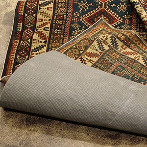 May include: A patterned rug with a dark blue background and intricate designs in red, yellow, and white. The rug is folded over a gray rug pad.