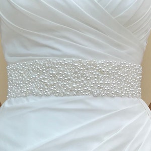 May include: A white satin wedding dress with a pearl beaded belt.