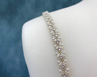 May include: A white and silver beaded strap with a geometric pattern of rhinestones. The strap is made of small white pearls and silver metal.