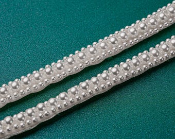 May include: White pearl trim with a satin ribbon backing. The trim is made of small, round pearls that are evenly spaced along the ribbon.