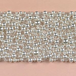 May include: A close-up of a white pearl trim with a variety of sizes of pearls.