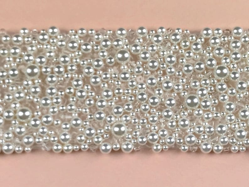 May include: A close-up of a white pearl trim with a variety of sizes of pearls.