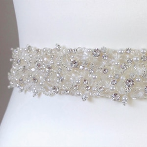 May include: A white beaded and rhinestone bridal belt with a delicate and intricate design.