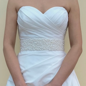 May include: A white strapless wedding dress with a pearl beaded belt.