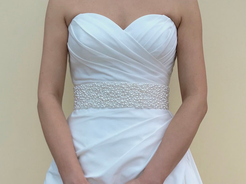 May include: A white strapless wedding dress with a pearl beaded belt.
