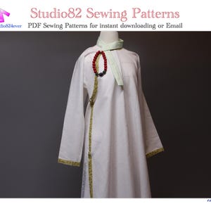 May include: A white garment with long sleeves and gold trim, displayed on a mannequin. The garment has a light green collar and a red and black beaded necklace. Text on the image reads "Studio82 Sewing Patterns".