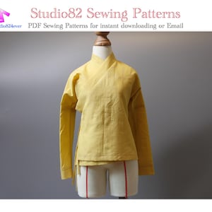 May include: A yellow wrap-style top displayed on a mannequin. The long-sleeved garment has a mandarin collar and a side tie closure. The image includes text that reads "Studio82 Sewing Patterns".