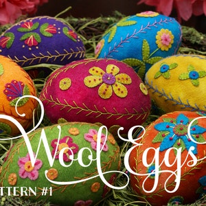 May include: Six colorful felt Easter eggs with embroidered floral designs. The eggs are arranged in a nest of straw. The text "Wool Eggs" is written in a decorative font across the front of the image. The text "PATTERN #1" is written in the bottom left corner of the image.
