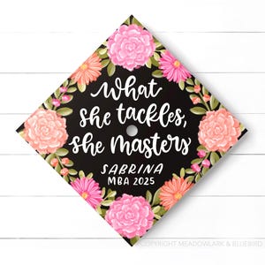May include: A graduation cap with a black background and floral design. The cap features the text "What she tackles, she masters" in white script, along with the name "Sabrina" and "MBA 2025". Pink and orange flowers surround the edges.