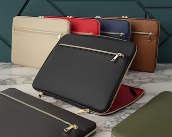 Puede incluir: Una colección de fundas rectangulares para portátiles en varios colores, incluyendo negro, beige, rojo, azul marino, marrón y verde oliva. Cada funda cuenta con un bolsillo frontal con cremallera, una cremallera principal y un forro interior.