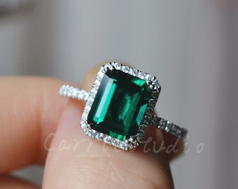 May include: A silver ring with a large emerald green gemstone surrounded by smaller clear gemstones.