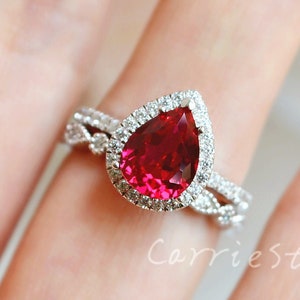 Puede incluir: Un anillo de rubí en forma de pera con un halo de diamantes más pequeños. El anillo está engastado en plata y tiene una banda delicada y retorcida.