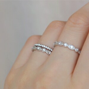 May include: Two silver rings with small clear stones. The top ring has a delicate, wavy design. The bottom ring has a simple, straight design.