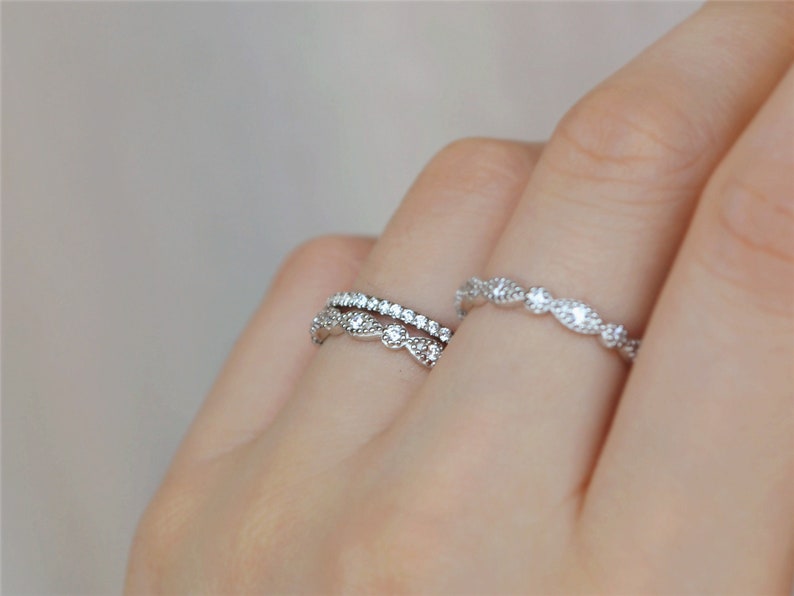 May include: Two silver rings with small clear stones. The top ring has a delicate, wavy design. The bottom ring has a simple, straight design.
