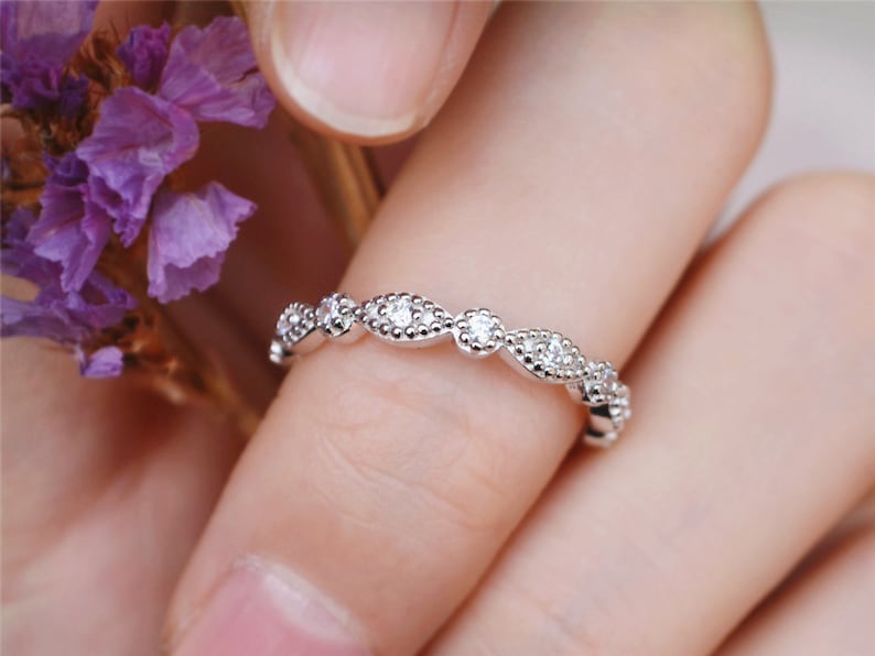 May include: A delicate silver band with a row of small, round diamonds set in a wavy pattern.