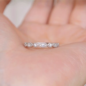 May include: A delicate silver band ring with a row of small, oval-shaped clear stones set in a pave setting.