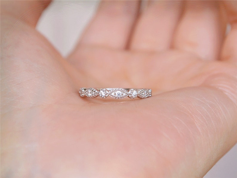 May include: A delicate silver band ring with a row of small, oval-shaped clear stones set in a pave setting.