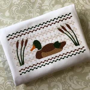May include: White fabric with a brown, green, and orange embroidered design of a duck swimming in a pond with cattails.