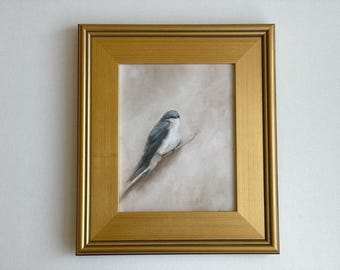 May include: A framed painting of a small bird with gray and white plumage perched on a branch. The artwork is set against a neutral background and enclosed in a gold-colored wooden frame.