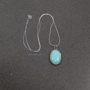 May include: A silver chain necklace with a pendant featuring a light blue oval gemstone.