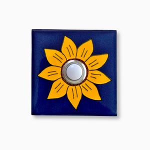 May include: A blue square ceramic doorbell button with a yellow sunflower design. The doorbell button has a white round button in the center.