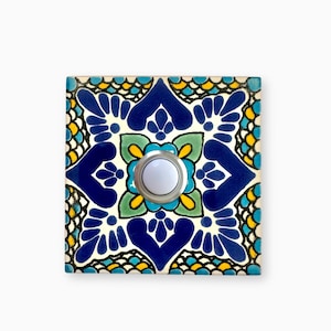 May include: A white ceramic doorbell button with a blue, yellow, and green patterned tile surround.