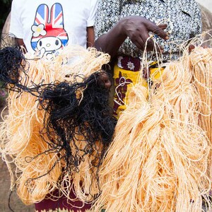 May include: Two people holding bundles of natural fiber yarn. One bundle is black and the other is a light orange color.