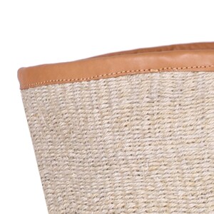 May include: A woven basket with a tan leather rim. The basket is made of natural fibers and has a natural, rustic look.
