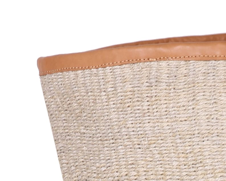 May include: A woven basket with a tan leather rim. The basket is made of natural fibers and has a natural, rustic look.