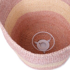 May include: A pink and beige woven basket with a white metal ring inside. The basket is made of natural fibers and has a striped pattern.