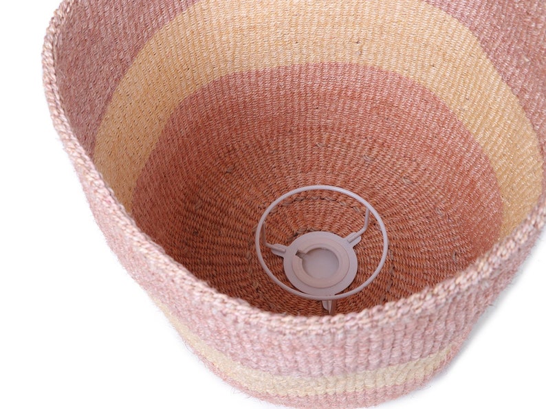 May include: A pink and beige woven basket with a white metal ring inside. The basket is made of natural fibers and has a striped pattern.