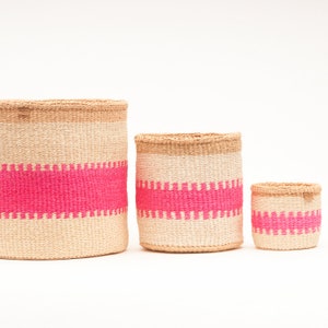 Puede incluir: Tres cestas tejidas con rayas rosas. Las cestas están hechas de materiales naturales y son de diferentes tamaños.