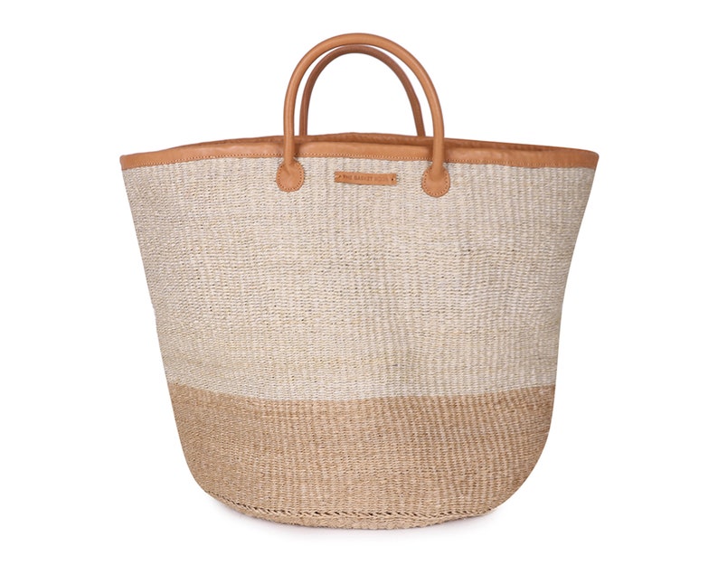May include: A large, woven tote bag with tan leather handles and a tan leather trim. The bag is made of natural fibers and has a two-toned design with a lighter top and a darker bottom.