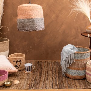 May include: A collection of woven baskets in various sizes and colors, including pink, brown, and blue, with a pink pillow and a seashell on a woven rug.