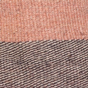 May include: Close-up of a woven basket with a pink and brown pattern. The basket is made of natural fibers and has a textured surface.