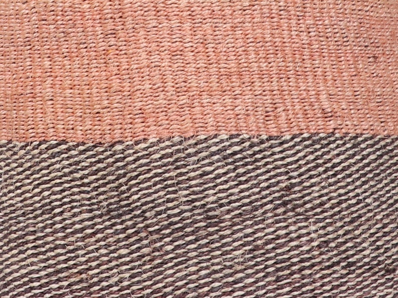 May include: Close-up of a woven basket with a pink and brown pattern. The basket is made of natural fibers and has a textured surface.