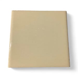 Pode incluir: Uma telha de cerâmica bege quadrada com um acabamento brilhante. A telha é de cor sólida e parece nova. As bordas são ligeiramente arredondadas. A telha tem aproximadamente 15 cm por 15 cm.