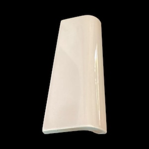 May include: A single, off-white ceramic tile with a curved edge and a glossy finish. The tile is rectangular with a slightly trapezoidal shape, and is set against a black background.