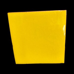 May include: A square, yellow ceramic tile with a glossy finish. The tile is a solid, vibrant yellow color and has a slightly textured surface. The edges are clean and well-defined, set against a black background.