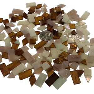 May include: A collection of small, irregularly shaped mosaic tiles in shades of white, brown, and pink. The tiles are scattered, with a US quarter for size reference. Ideal for craft projects.