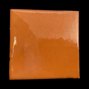 May include: Square orange ceramic tile with a glossy finish. The tile has a smooth surface and a slightly rounded edge. The colour is a warm, vibrant orange, and the tile is set against a black background.