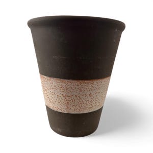 Puede incluir: Una taza de cerámica marrón oscuro con una banda texturizada blanquecina. La taza tiene una forma ligeramente cónica y un borde liso. La banda tiene un aspecto moteado, lo que añade interés visual al diseño. La taza es probablemente para bebidas.