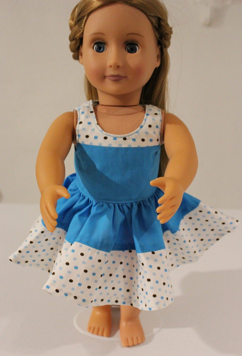 Puede incluir: Un vestido de lunares azules y blancos con un corpi&ntilde;o azul y una falda blanca. El vestido es sin mangas y tiene un escote redondo. La mu&ntilde;eca lleva el vestido y tiene el pelo rubio.