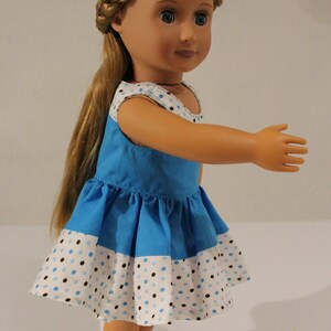 Puede incluir: Una mu&ntilde;eca con un vestido de lunares azules y blancos, con un corpi&ntilde;o azul y una falda blanca. La mu&ntilde;eca tiene el pelo largo y rubio y los ojos azules.