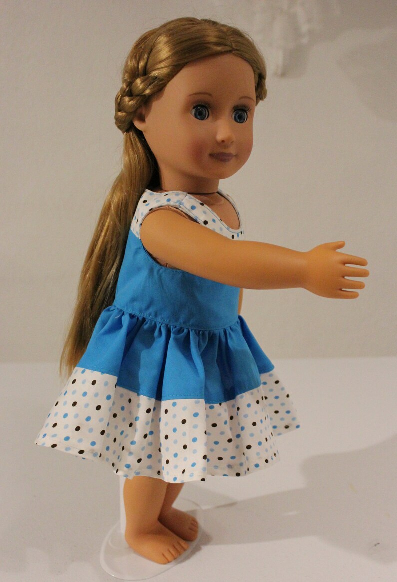 Puede incluir: Una mu&ntilde;eca con un vestido de lunares azules y blancos, con un corpi&ntilde;o azul y una falda blanca. La mu&ntilde;eca tiene el pelo largo y rubio y los ojos azules.