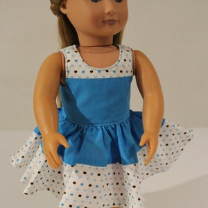 Puede incluir: Una mu&ntilde;eca con un vestido de lunares azules y blancos con ribete marr&oacute;n. El vestido tiene un corpi&ntilde;o azul y una falda blanca con lunares marrones.