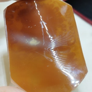 May include: A smooth, polished, orange agate stone with white veins and a translucent appearance.